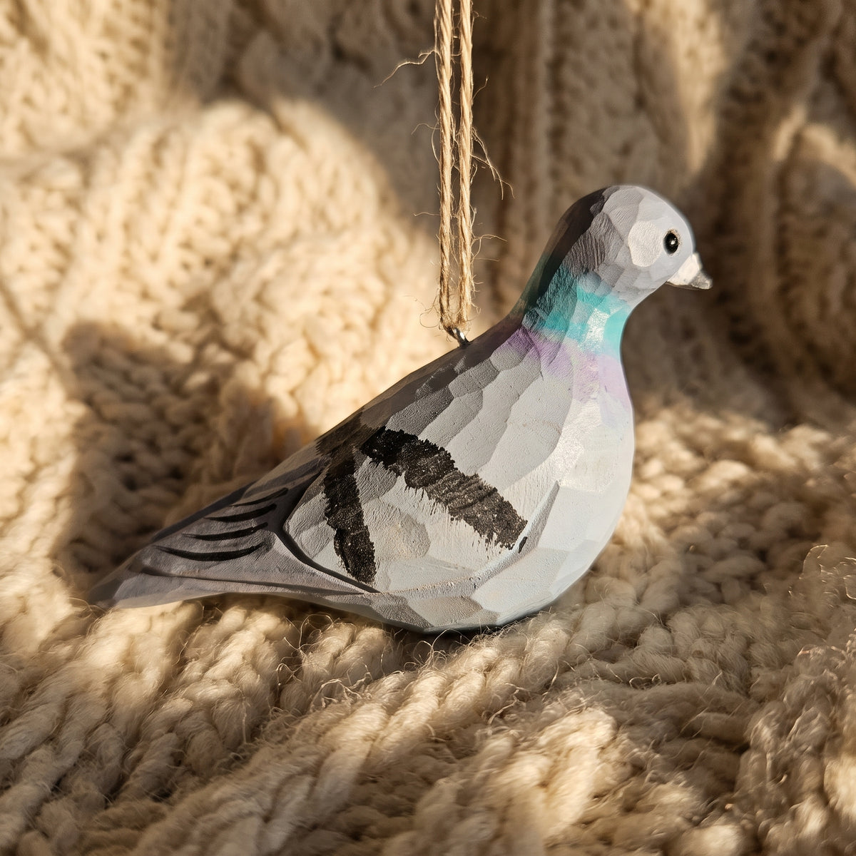 Hand-carved wooden Rock Dove pigeon ornament resting on a warm, textured beige knit background in soft sunlight.