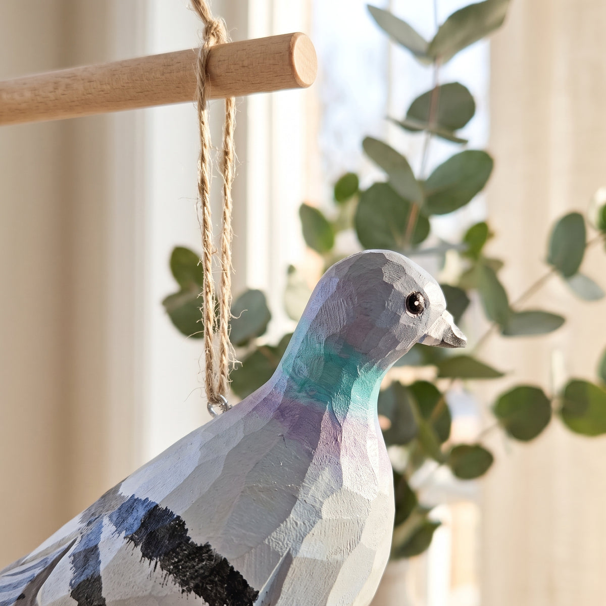 Close-up profile of a hand-carved wooden Rock Dove pigeon ornament with painted green and purple neck details, hanging from a twine string.