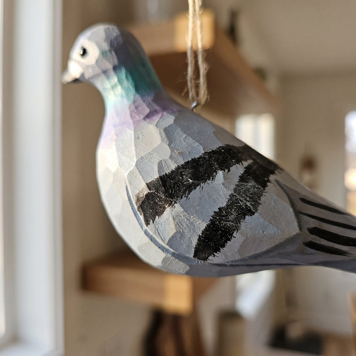 Side view of a hand-carved wooden Rock Dove pigeon ornament showing detailed wood grain textures, black wing bars, and a painted green neck accent.