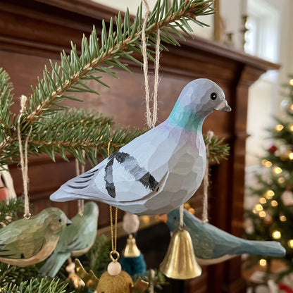 Hand-carved and hand-painted wooden Rock Dove pigeon ornament hanging from a pine branch in front of a cozy holiday fireplace.