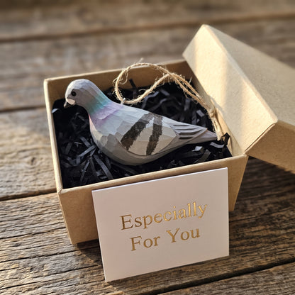 Hand-carved wooden Rock Dove pigeon ornament resting inside an open kraft gift box with a card reading "Especially For You".