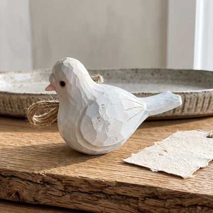 Hand-carved white wooden baby pigeon hanging ornament on a wooden surface.
