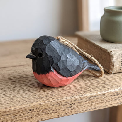 Hand-carved wooden pink robin ornament with a twine loop resting on a wooden table.