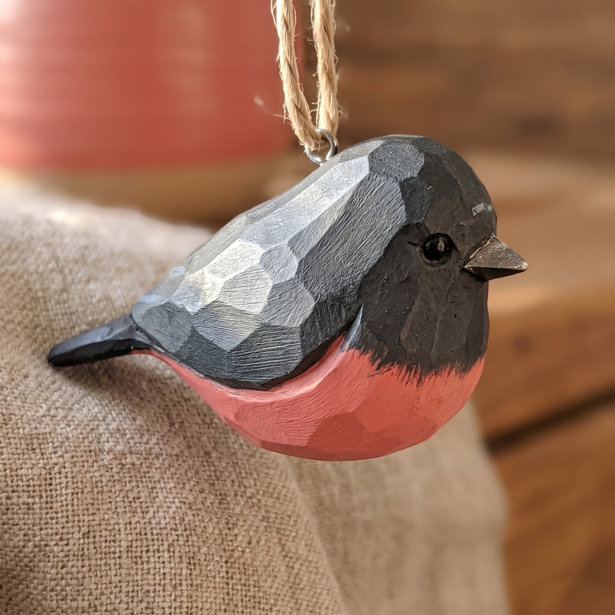 Close-up of a hand-carved wooden pink robin ornament resting on burlap fabric.