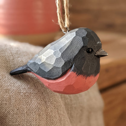 Close-up of a hand-carved wooden pink robin ornament resting on burlap fabric.