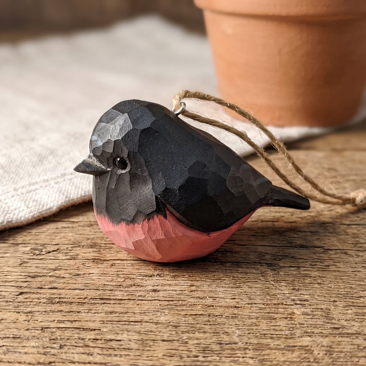 Hand-carved wooden pink robin ornament resting on a rustic wooden table.