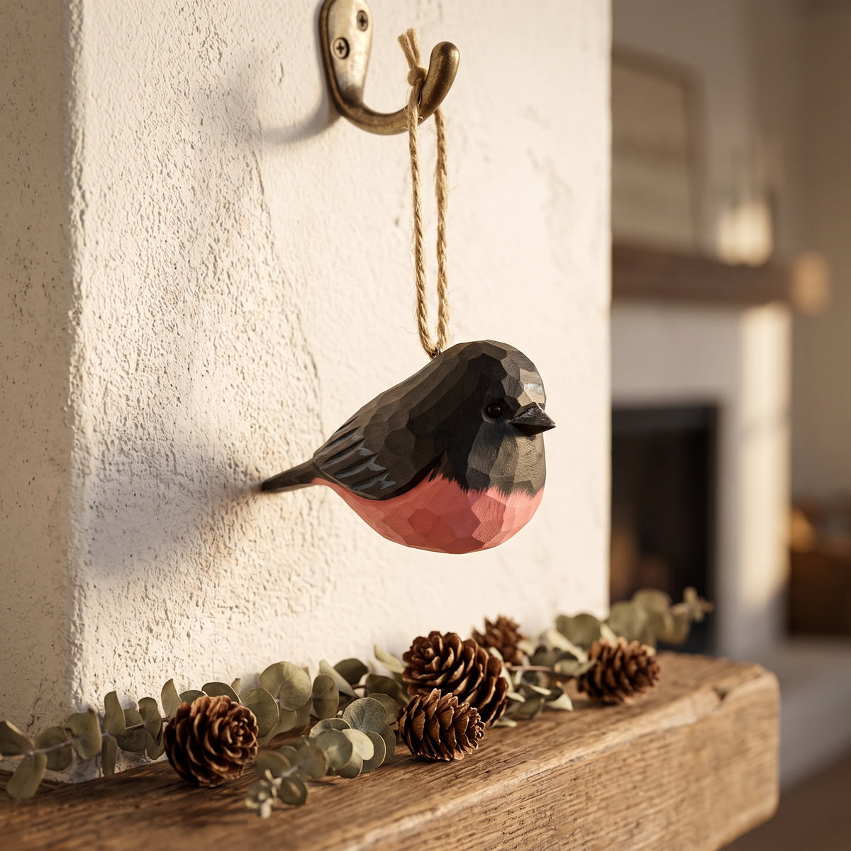 Hand-carved basswood pink robin hanging Christmas tree ornament on a wall hook over a fireplace mantel.