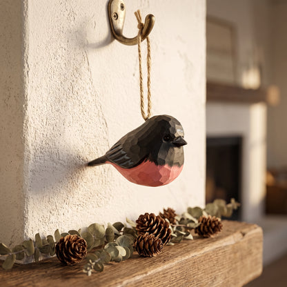 Hand-carved basswood pink robin hanging Christmas tree ornament on a wall hook over a fireplace mantel.