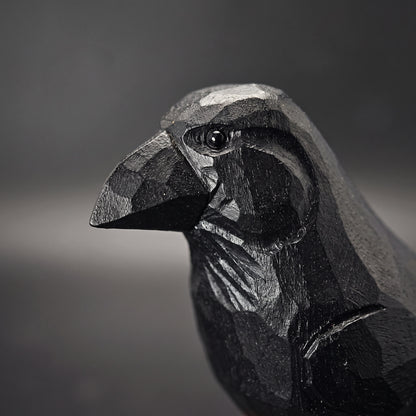 Close-up of a black carved Raven sculpture, showing detailed facets and texture on its beak and head against a dark gray background.