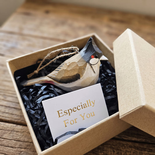 A handcrafted wooden Red-whiskered bulbul ornament nestled in black crinkle paper inside a kraft gift box, with a small card reading 'Especially For You' on a rustic wooden table.