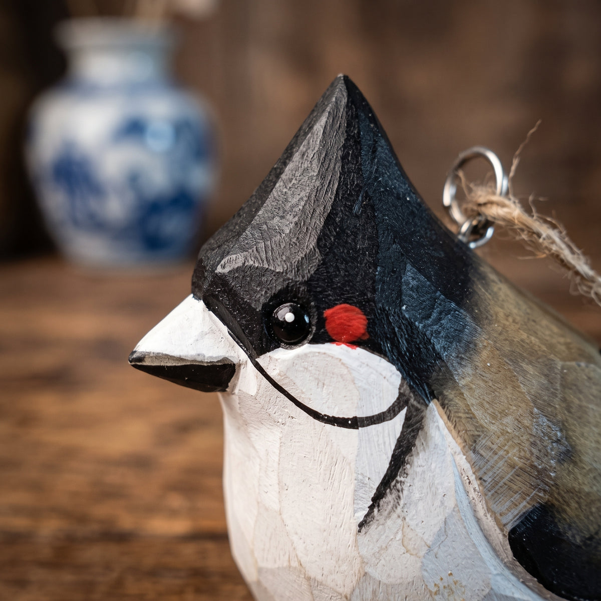 A close-up of a carved wooden Red-whiskered bulbul ornament, likely a crested bird, with a black, white, and gray painted finish, a small red accent, and a metal hanging loop.
