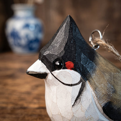 A close-up of a carved wooden Red-whiskered bulbul ornament, likely a crested bird, with a black, white, and gray painted finish, a small red accent, and a metal hanging loop.