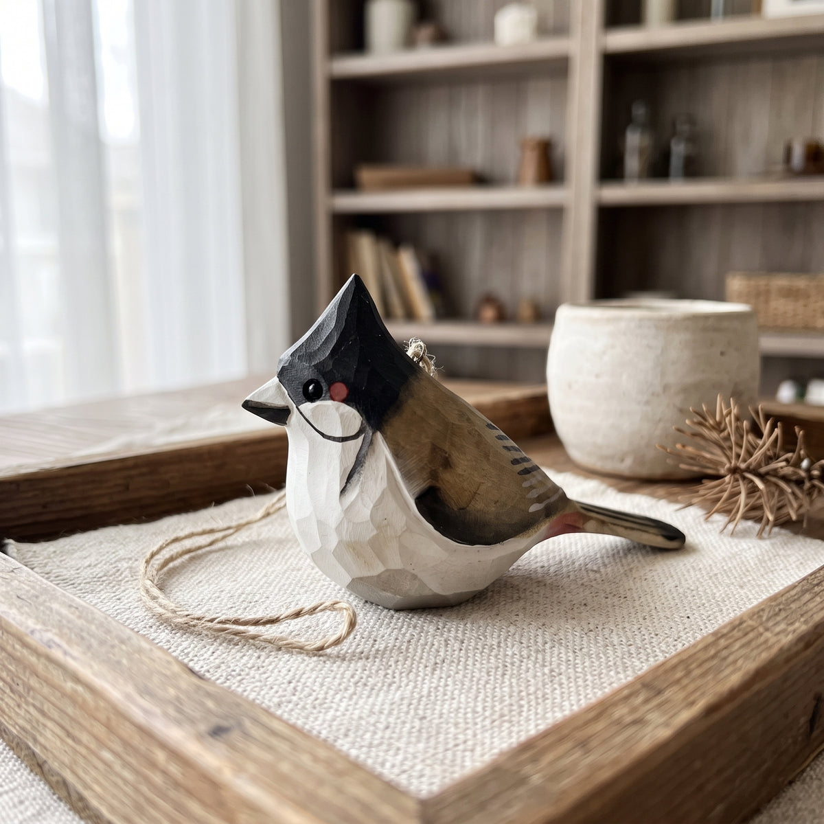 A faceted Red-whiskered bulbul-shaped wall hanging ornament with a black, white, and brown color scheme, resting on a burlap-covered wooden tray in a rustic room setting.