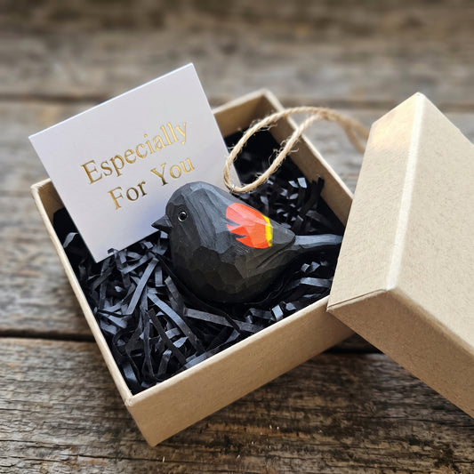 Hand-carved wooden Red-Winged Blackbird hanging ornament packaged in an open kraft gift box with shredded paper fill and an "Especially For You" card.
