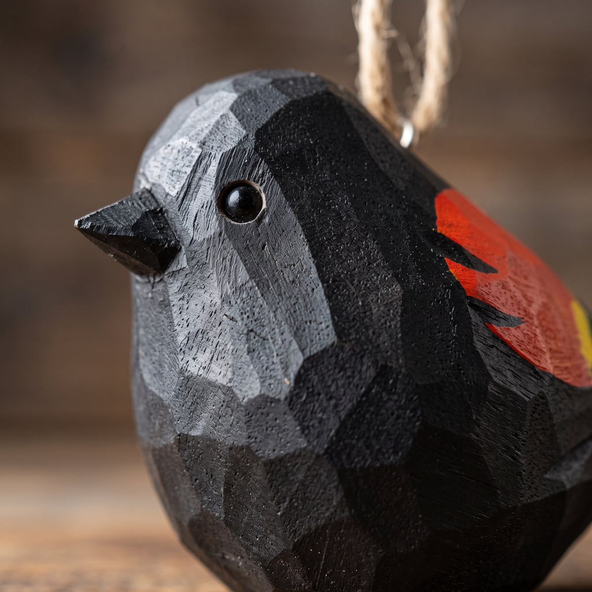 Close-up macro shot of a hand-carved wooden Red-Winged Blackbird ornament highlighting the faceted chiseled wood texture and red and yellow wing accents.
