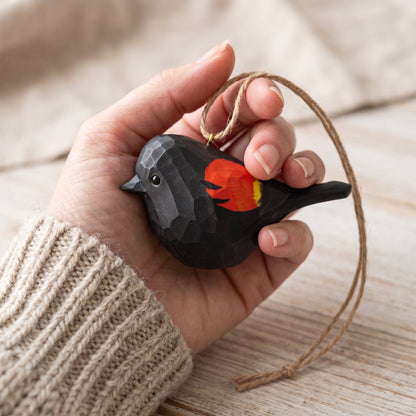 Hand-carved wooden Red-Winged Blackbird hanging ornament held in a hand wearing a cozy knit sweater.