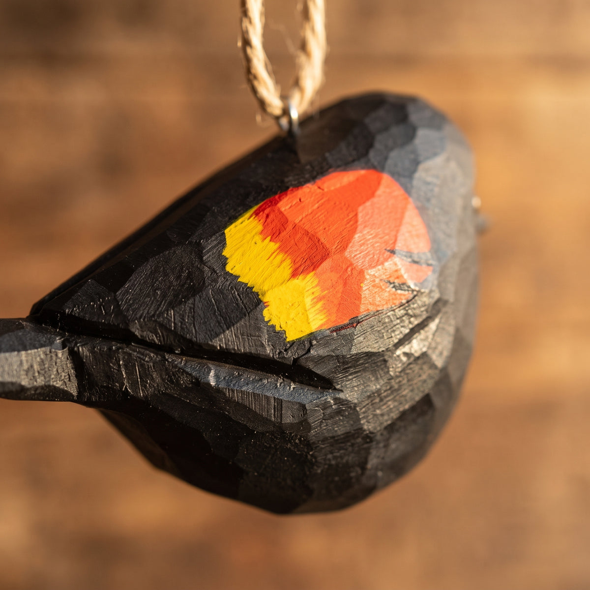 Extreme close-up of a hand-carved wooden Red-Winged Blackbird ornament highlighting the faceted chiseled wood grain and vibrant hand-painted red, orange, and yellow wing patch.