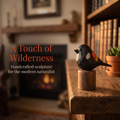 A handcrafted wooden Red-winged blackbird sculpture with geometric facets in black, white, orange, and red, mounted on a round wooden base and displayed on a rustic wooden table in a cozy, warmly lit room with a blurred fireplace and bookshelves in the background. Text on the left reads 'A Touch of Wilderness: Handcrafted sculpture for the modern naturalist'.