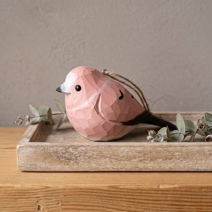 A pink geometric Rosefinch ornament with a black beak and tail, displayed on a rustic wooden tray with dried greenery against a neutral background.