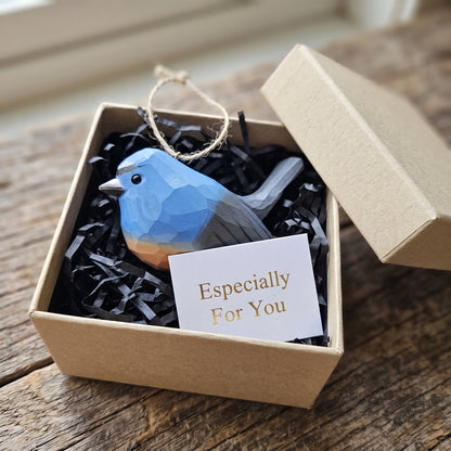 A faceted Snowy-browed flycatcher-shaped ornament in blue, gray, and orange is presented in a kraft gift box with black shredded paper filler and a small card that reads 'Especially For You.'.