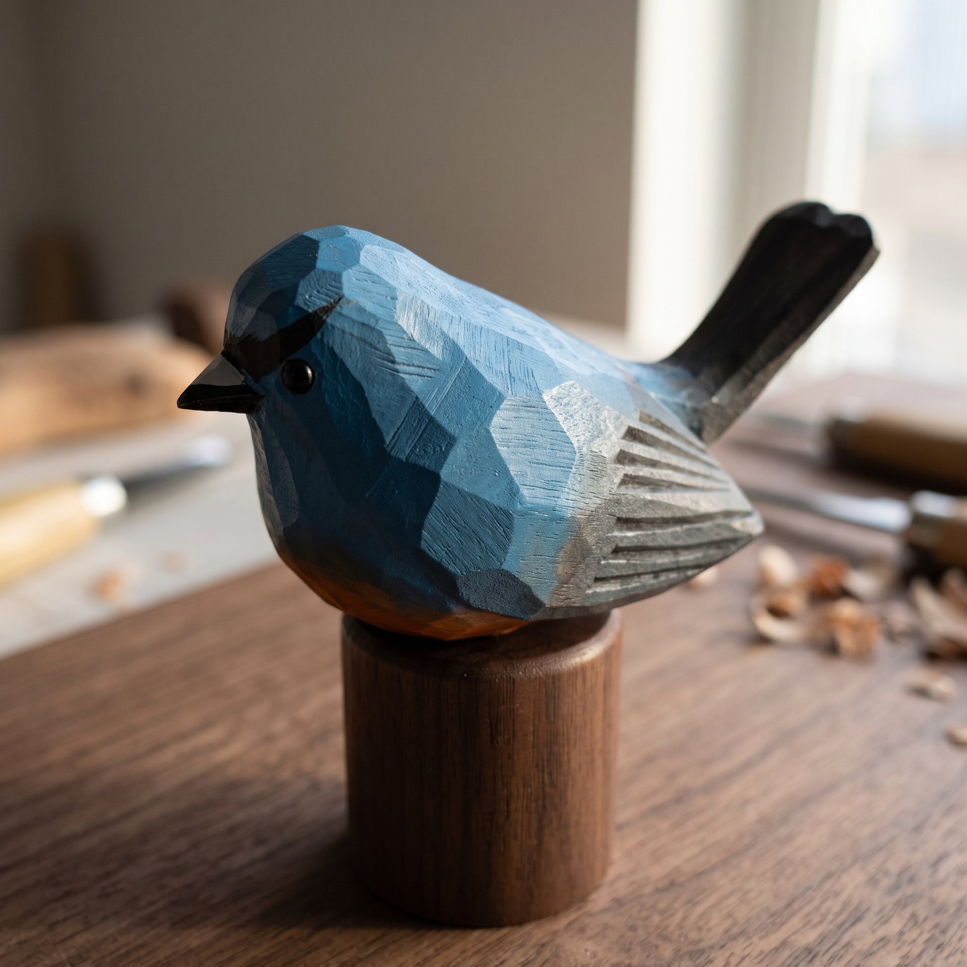 A hand-carved wooden Snowy-browed flycatcher sculpture with geometric facets in shades of blue, gray, and black, mounted on a cylindrical wooden base on a wooden table.