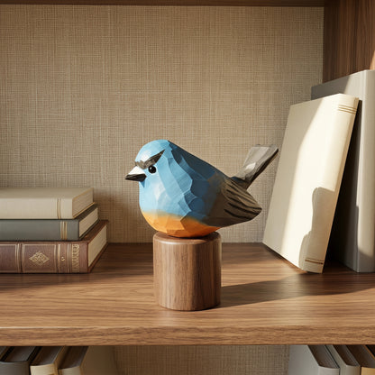 A geometric Snowy-browed flycatcher figurine with a blue, gray, and orange color scheme, displayed on a wooden cylinder stand on a wooden shelf next to books.