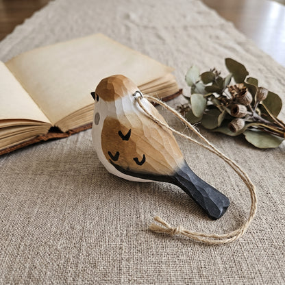 Hand-carved basswood sparrow ornament with jute string lying on a linen runner beside an open book