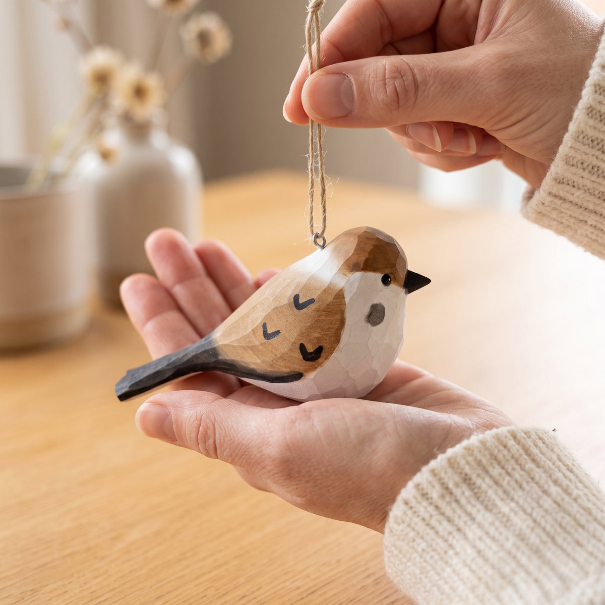 Hand holding a hand-carved basswood sparrow ornament by its twine hanging string