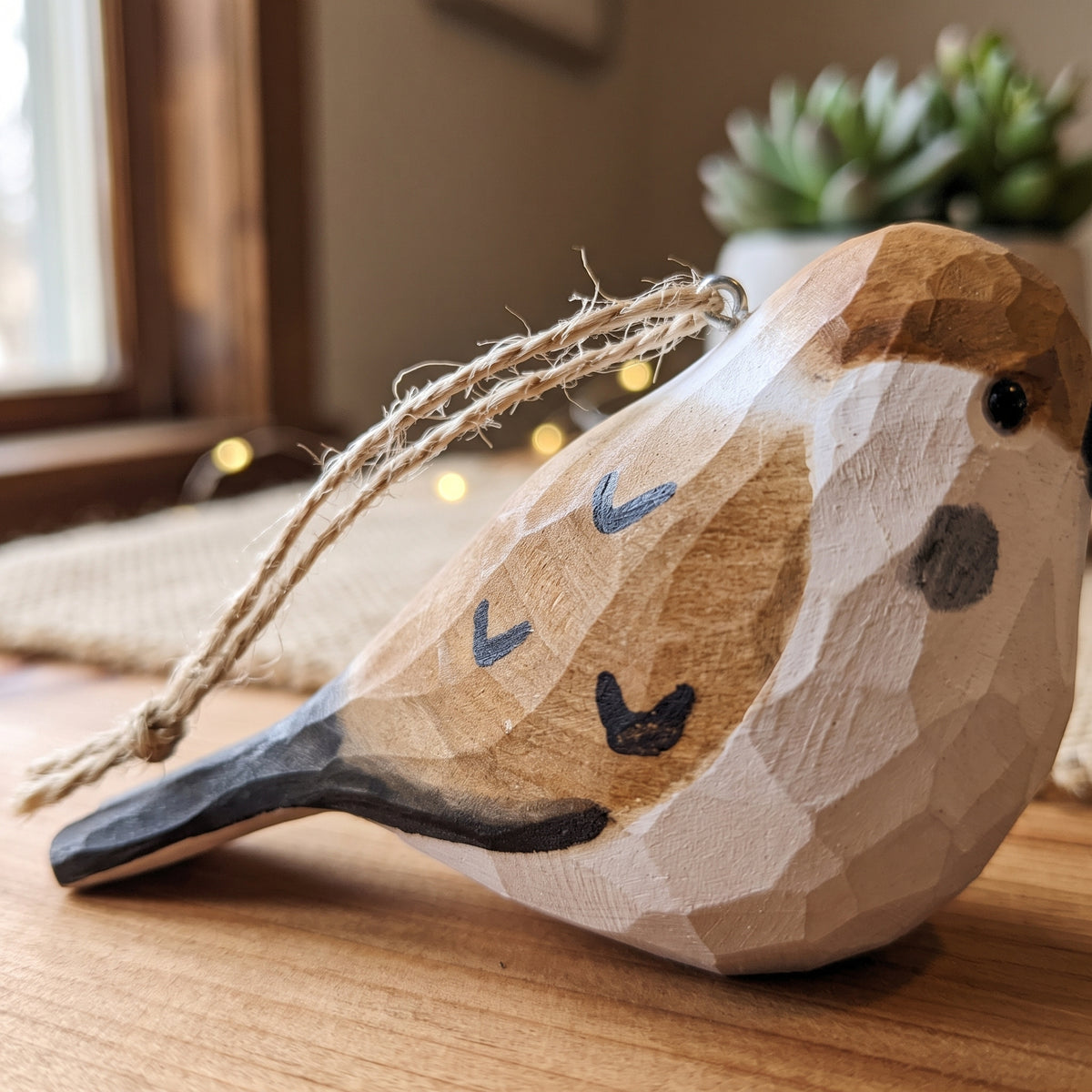 Hand-carved basswood sparrow ornament resting on a wooden table showing hand-painted feather details and twine loop