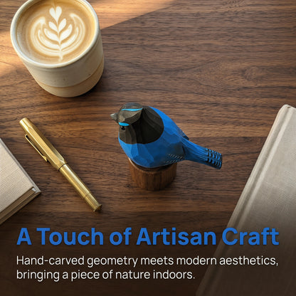 A blue and black geometric stellers jay figurine displayed on a wooden desk alongside a cup of latte, a gold pen, and books, with the text 'A Touch of Artisan Craft' overlaid at the bottom.
