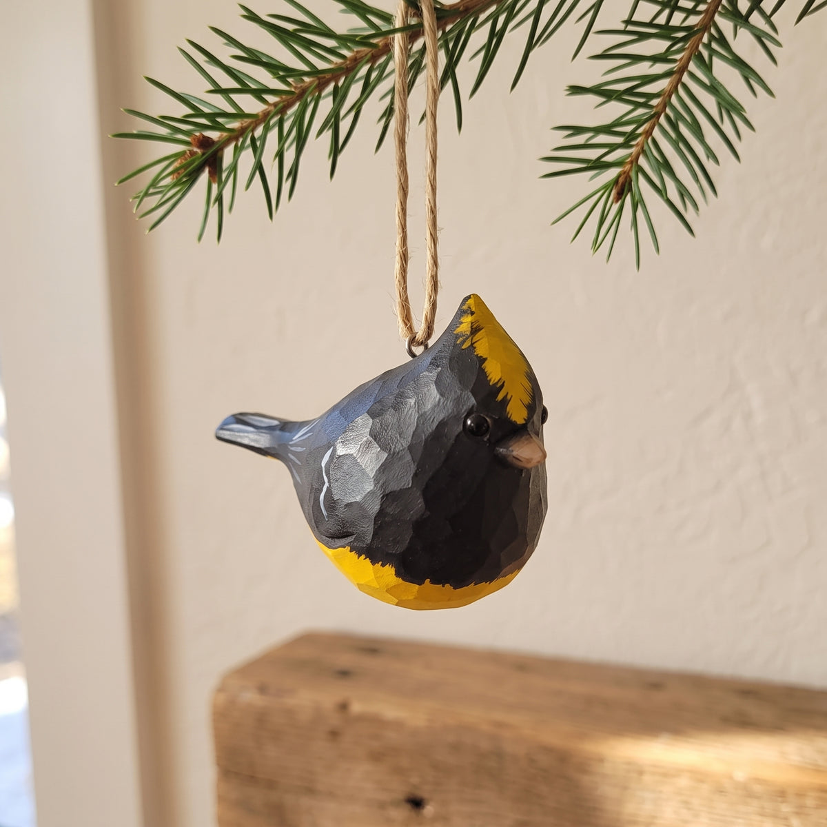 Hand-carved wooden Sultan Tit bird ornament hanging from a pine branch