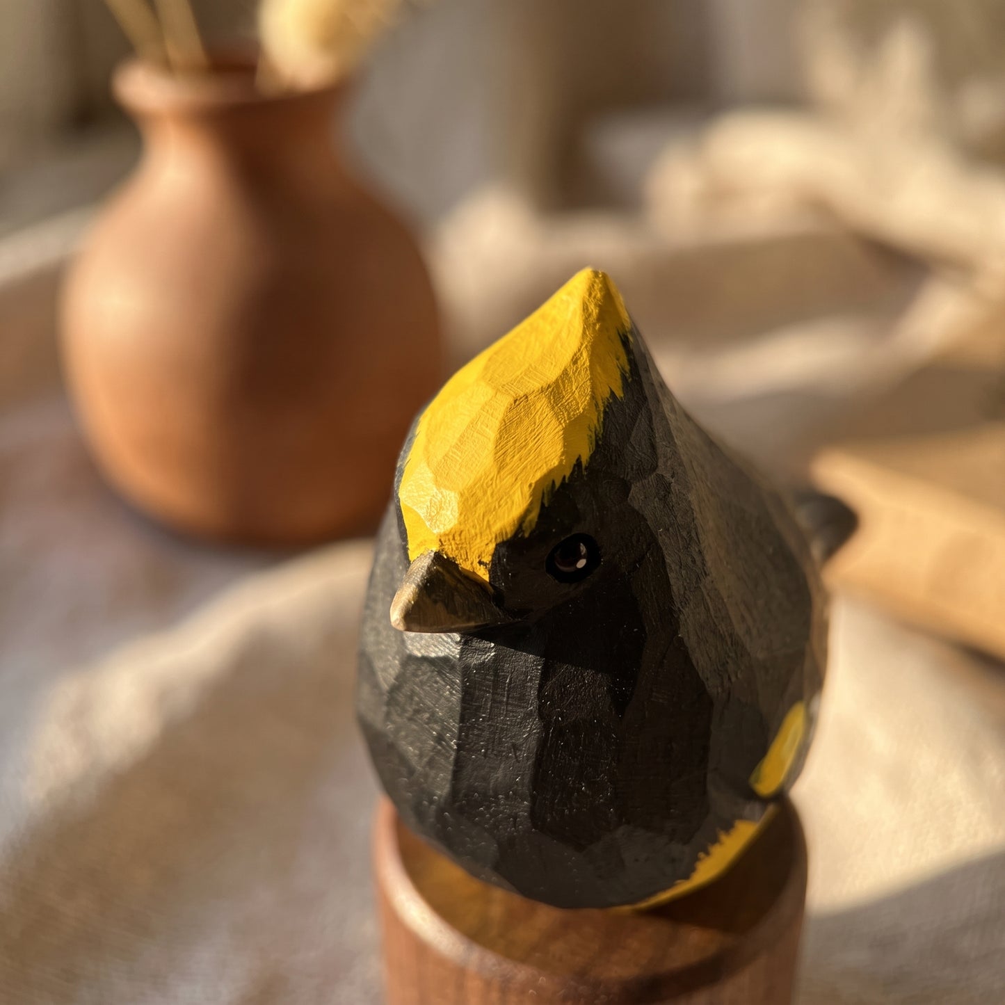 A hand-carved wooden Sultan tit figurine with a black and yellow painted finish, displayed on a wooden stand in a warm, softly lit setting.