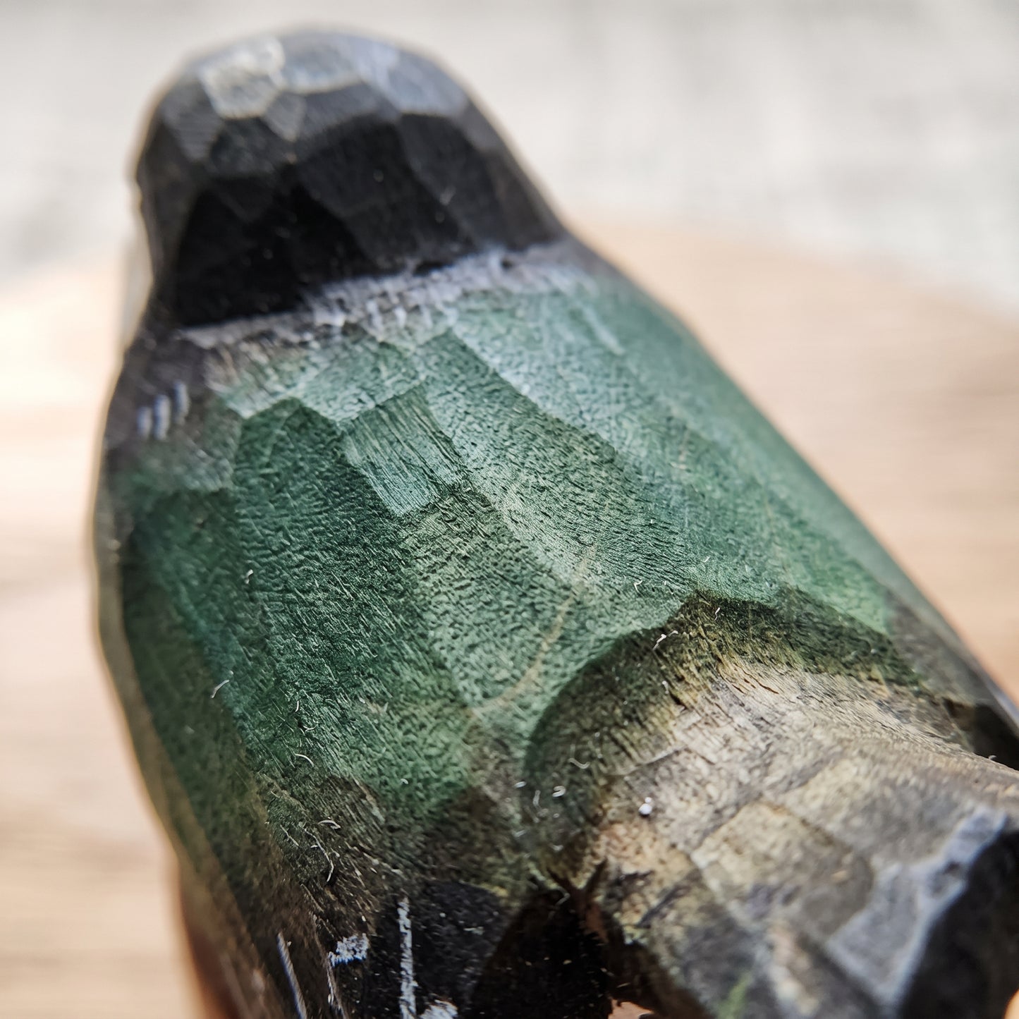 Close-up of a hand-carved wooden Swallow figurine with a textured green and black finish, resting on a light wooden surface.