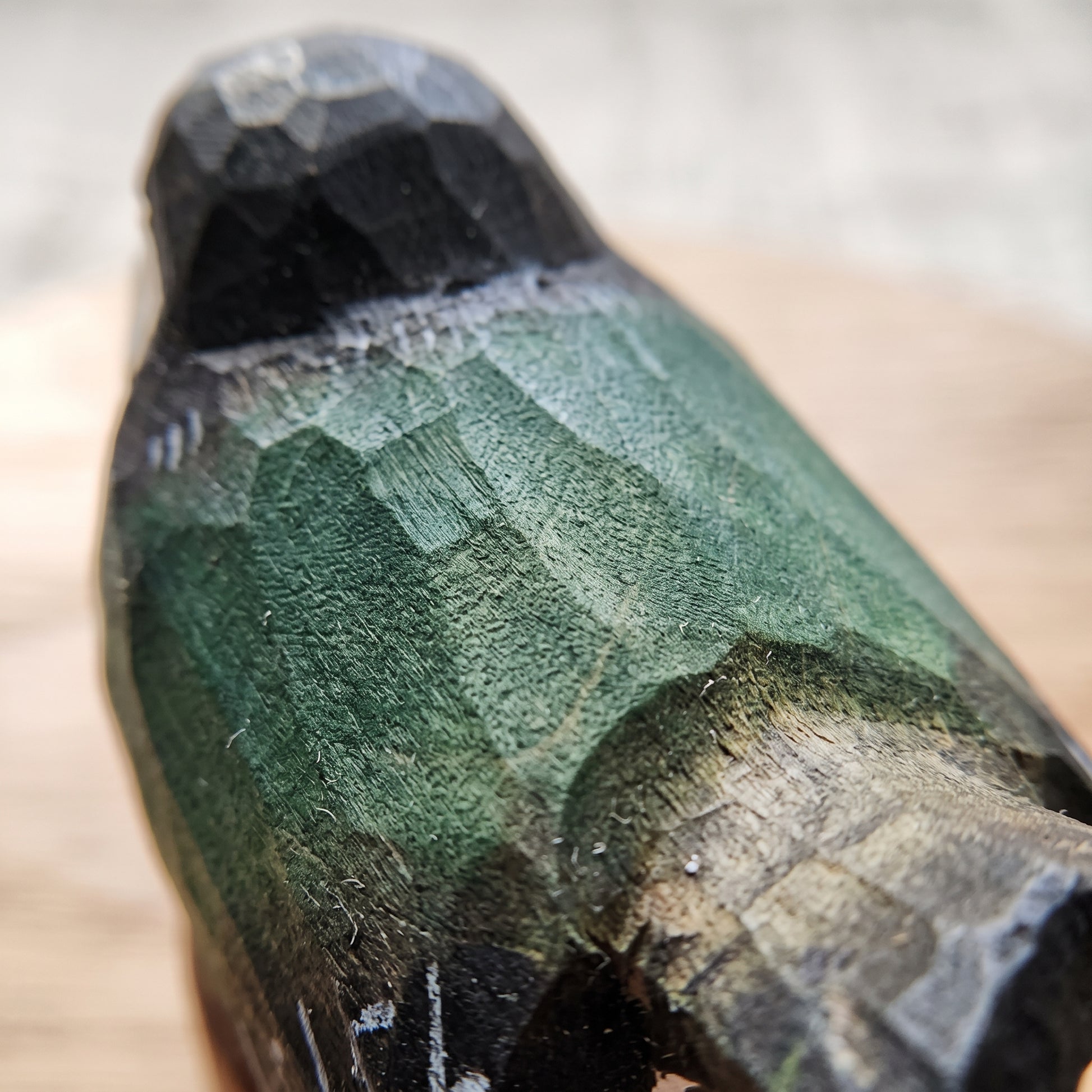 Close-up of a hand-carved wooden Swallow figurine with a textured green and black finish, resting on a light wooden surface.