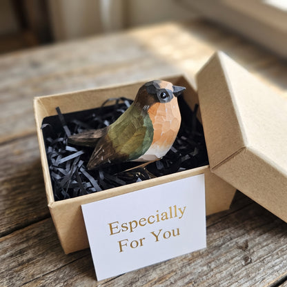 Side profile view of a hand-carved, hand-painted wooden Barn Swallow clip-on bird ornament sitting inside an open kraft gift box filled with black shredded paper, alongside a small white card reading 'Especially For You'.