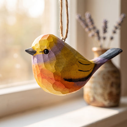 A handcrafted wooden White-browed tit-warbler ornament with a geometric, faceted finish, hanging by a twine loop in a warm, sunlit room next to a window and a vase of dried lavender.