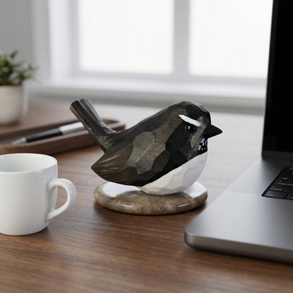 Hand-carved wooden Willie Wagtail figurine with black and white plumage sitting on a desk next to a laptop and coffee mug.