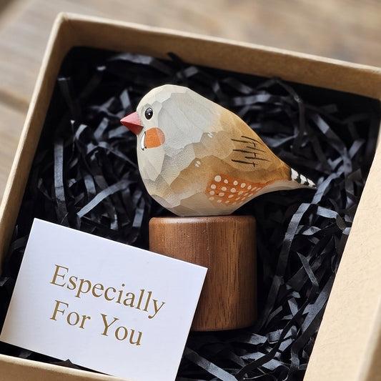 A small decorative Zebra Finch figurine with a wooden base sits in a kraft gift box filled with black shredded paper and a card that reads 'Especially For You,' placed on a rustic wooden surface.