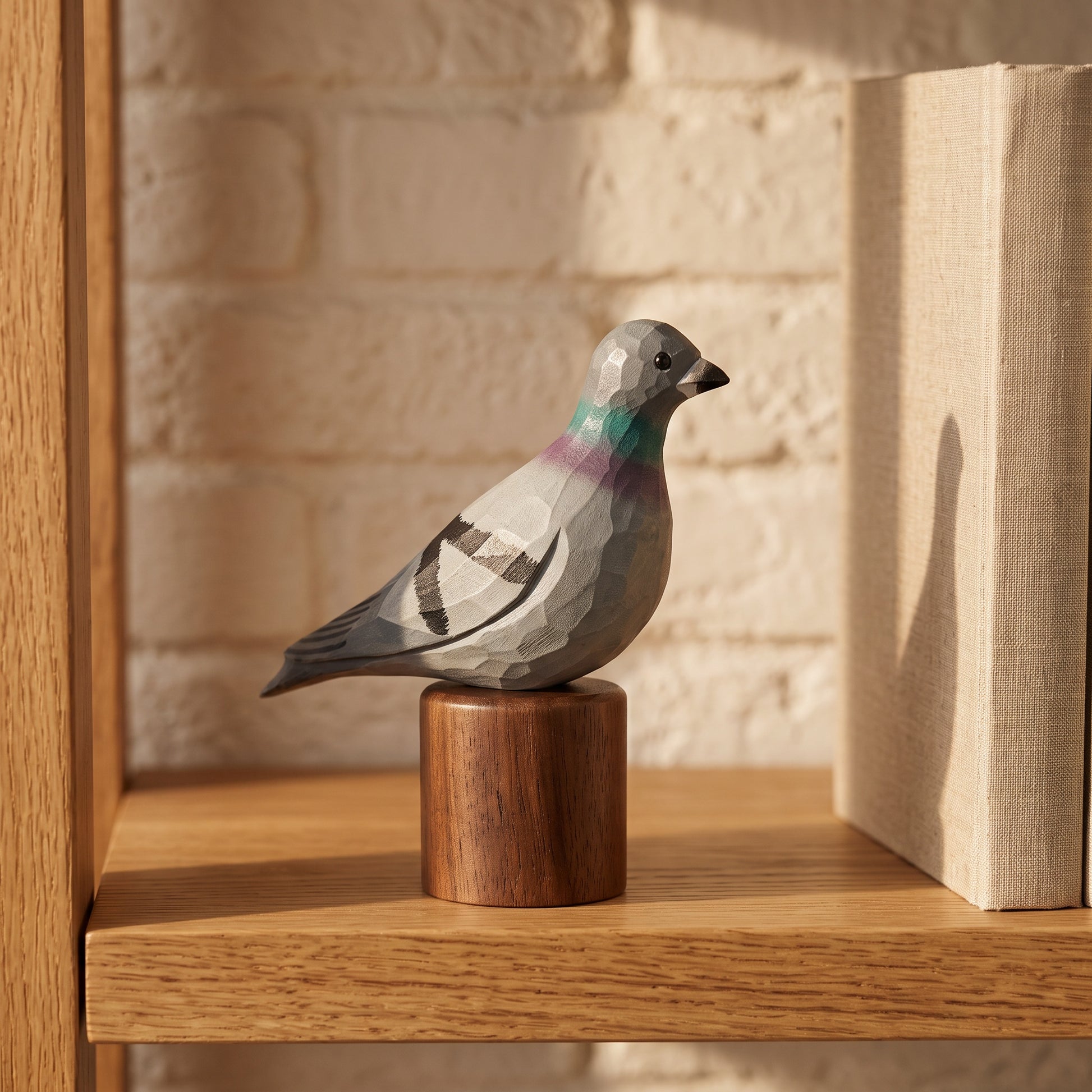 A geometric wooden Rock dove figurine with a faceted polygonal design, perched on a small cylindrical wooden base. The figurine features gray, black, and white panels with a purple and green iridescent neck detail.