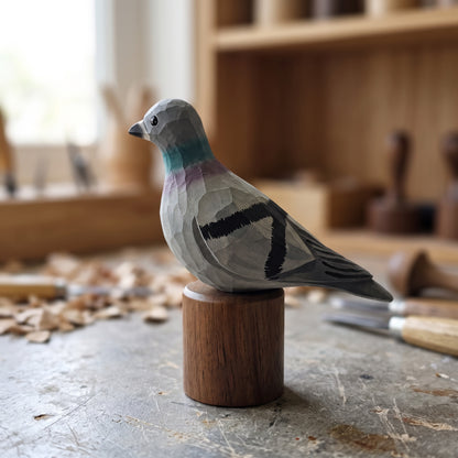A handcrafted wooden Rock dove sculpture with geometric facets, perched on a small cylindrical wooden base in a woodworking workshop.