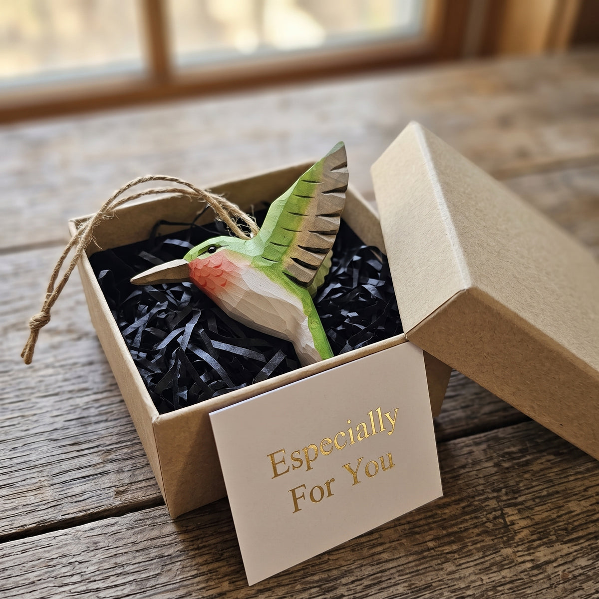 Green hand-carved basswood hummingbird ornament presented in a brown gift box with black paper fill.
