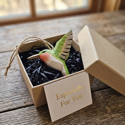 Green hand-carved basswood hummingbird ornament presented in a brown gift box with black paper fill.