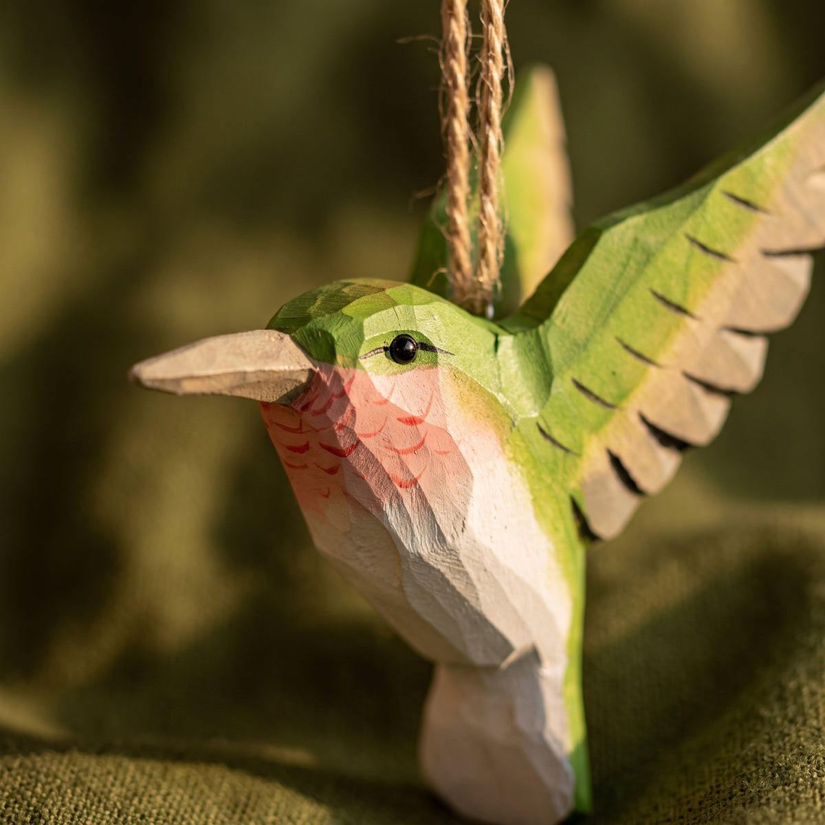 Detailed close-up of a green hand-carved basswood hummingbird hanging ornament showing carved throat accents and twine loop.