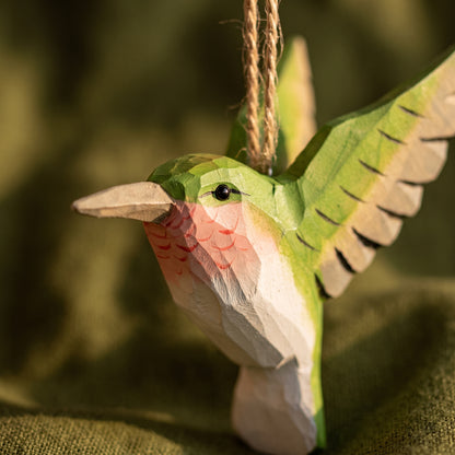 Detailed close-up of a green hand-carved basswood hummingbird hanging ornament showing carved throat accents and twine loop.