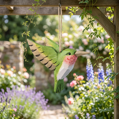 Green hand-carved basswood hummingbird hanging ornament displayed outdoors in a sunny garden setting.