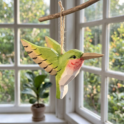 Green hand-carved basswood hummingbird hanging ornament displayed by a window.