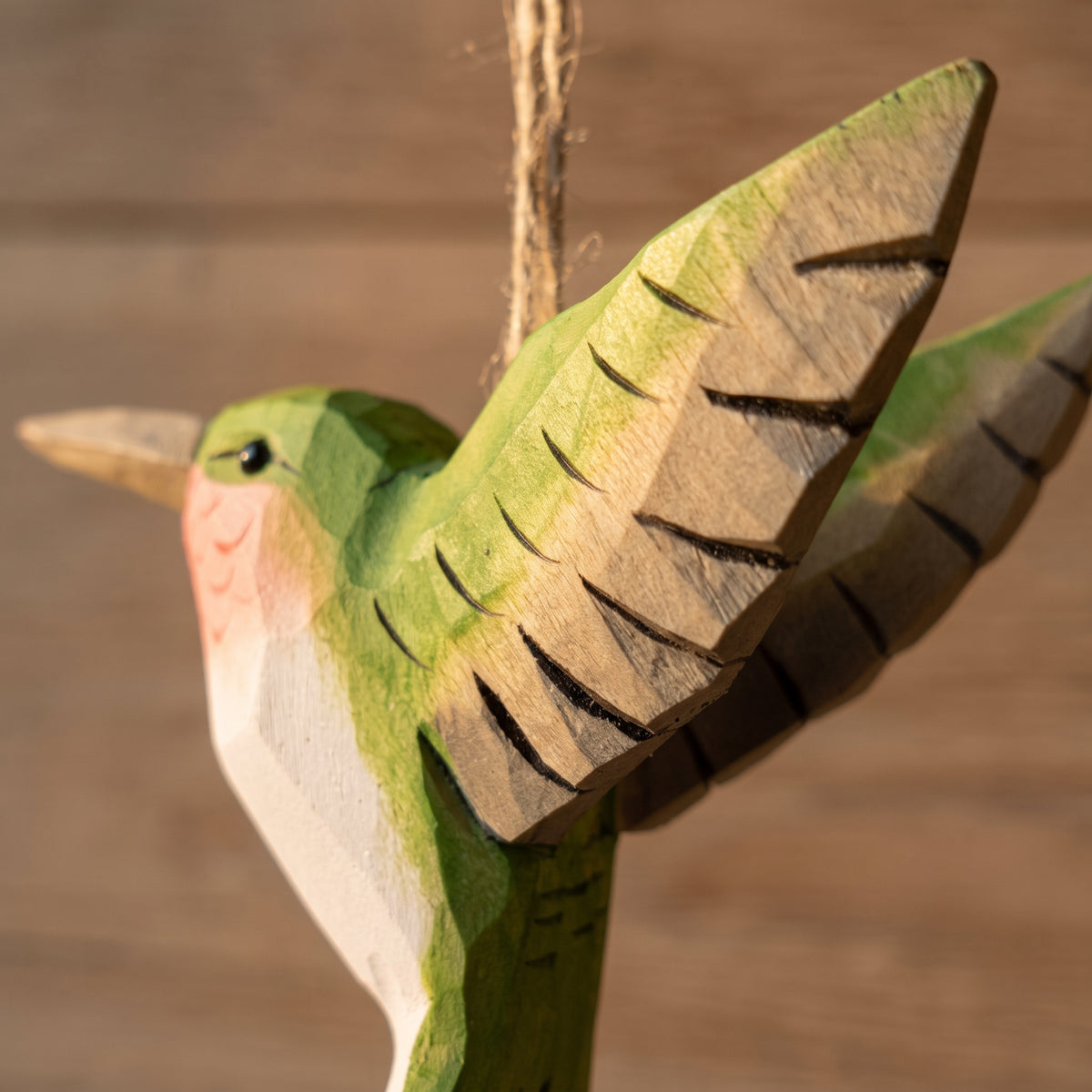 Detailed close-up of a green hand-carved basswood hummingbird hanging ornament highlighting carved wing details and twine loop.
