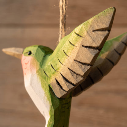 Detailed close-up of a green hand-carved basswood hummingbird hanging ornament highlighting carved wing details and twine loop.