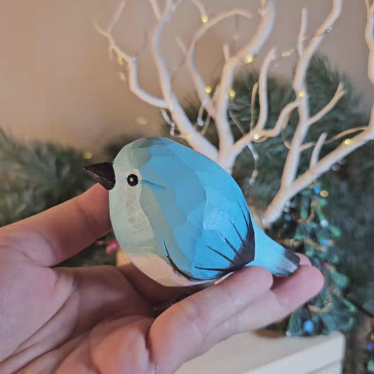 A hand-carved blue wooden bird ornament with a black beak held resting in an open palm.